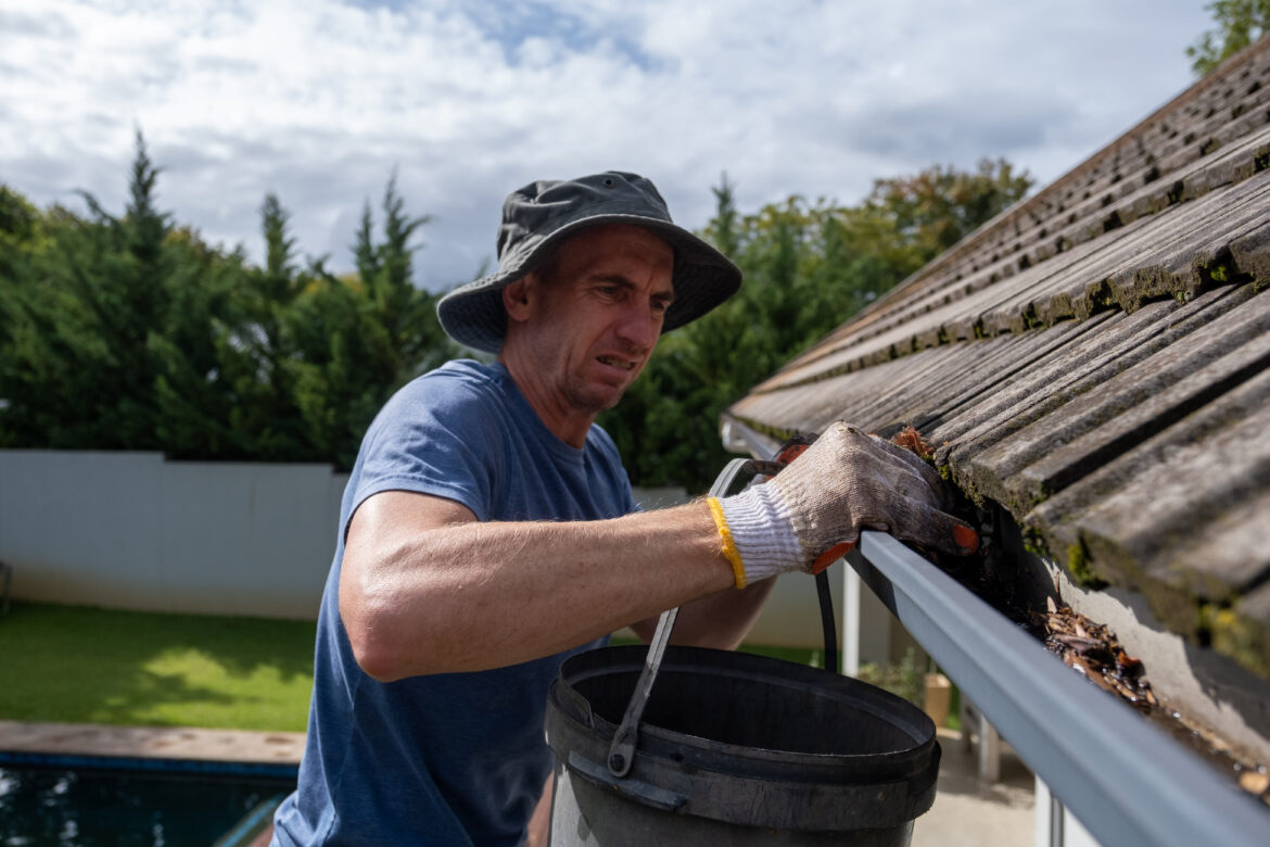 Man cleaning gutters of debris and leaves