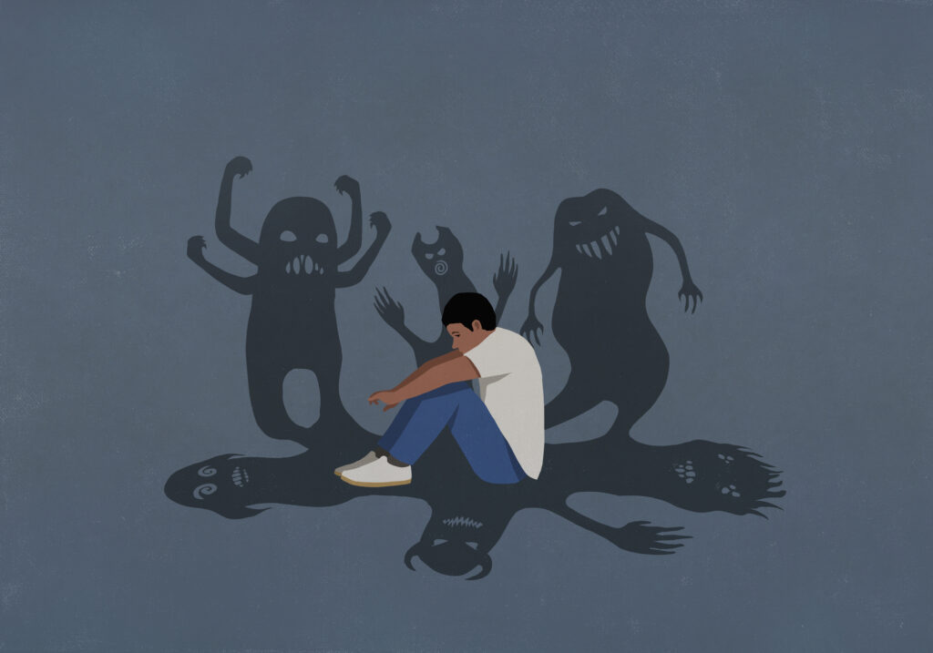 Shadows of monsters surrounding anxious teenage boy hugging knees