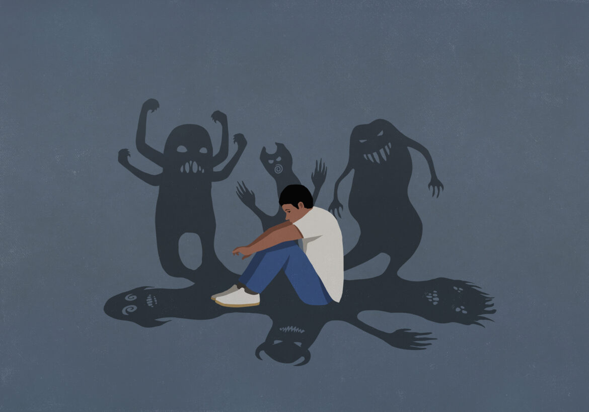 Shadows of monsters surrounding anxious teenage boy hugging knees